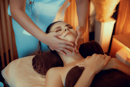 Caucasian woman enjoying relaxing anti-stress head massage and pampering facial beauty skin recreation leisure in warm candle lighting ambient salon spa in luxury resort or hotel. Quiescentの写真素材