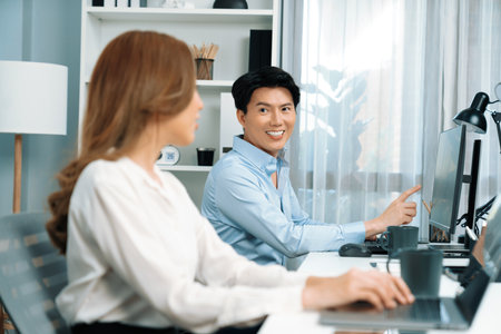 Smiling Asian man talking with woman colleague in planning marketing report project on laptop casual day while searching database on working desk at modern home office at side view image. Infobahn.の写真素材