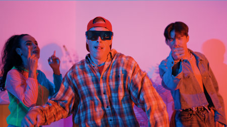 Hispanic hipster wear colorful cloth and waving to freestyle music. Professional break dancer moving to lively beat with neon light and led light with modern studio surrounded by friend. Regalement.の写真素材