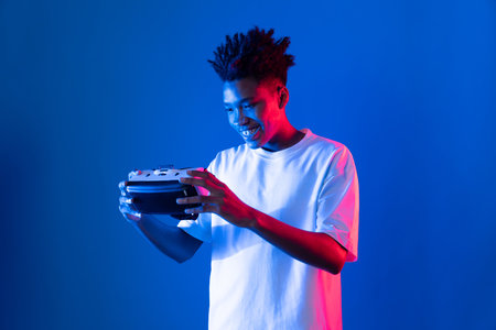 Surprised young African American looking through VR holding interesting object hologram on pink blue neon wall at metaverse world connecting digital futuristic technology virtual reality. Contrivance.の写真素材