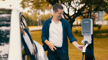 Man recharging battery for electric car during road trip travel EV car in autumanl season natural forest or national park. Eco friendly travel during vacation and holiday. Exaltの写真素材