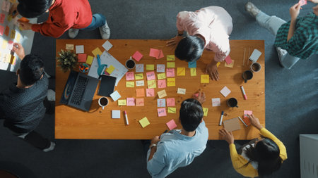 Top view of skilled business people discuss plan at meeting room while writing idea at sticky notes and stick at whiteboard. Group of diverse team working together to planning strategy. Convocation.の写真素材