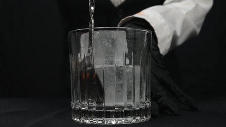 Macrography, observe the skilled hands of a female bartender expertly stirring ice in glass with ice at black background. Each close-up shot of woman prepare for making cocktail in glass. Comestible.の写真素材