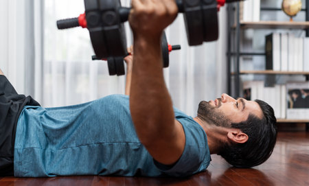 Athletic body and active sporty man lifting dumbbell weight for effective targeting muscle gain at gaiety home as concept of healthy fit body home workout lifestyle.の写真素材