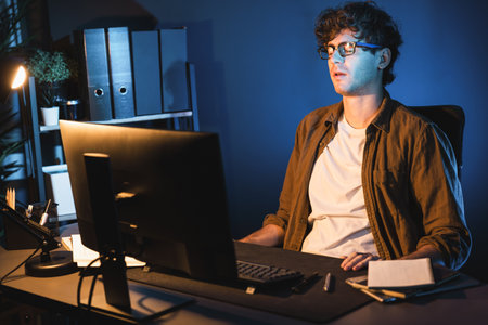 Stressful creative manager searching design thinking with new presentation while waiting email sending back on laptop screen at home office in casual shirt at neon light room at night time. Gusher.の写真素材