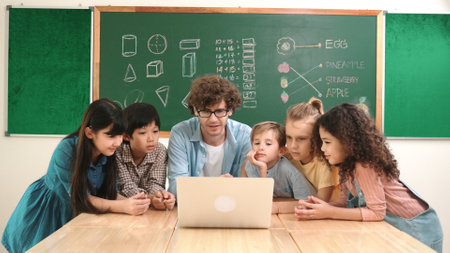 Caucasian teacher and diverse student looking at laptop at classroom. Cute multicultural children learning about coding program or generated program by using software while teacher teaching. Pedagogy.の写真素材