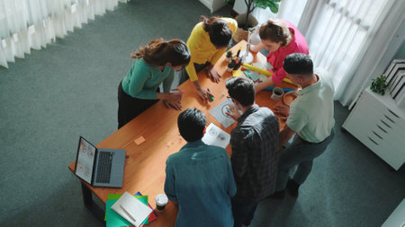 Top down aerial view of skilled designer hold logo while discuss with team. Aerial business group...