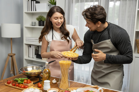 Couple chef influencers cooking special homemade of spaghetti with tongs taking to frying pan, putting seasoning and tasty sauce to make good flavor, recording on camera with live chanel. Postulate.の写真素材