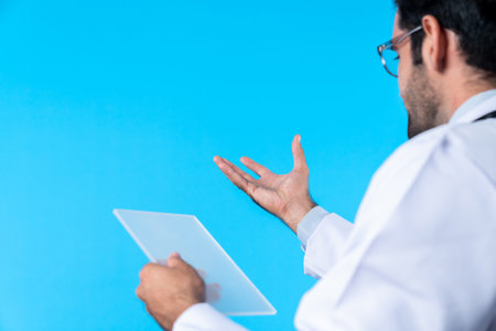 Back view of smart doctor looking application form while standing at blue background. Professional...