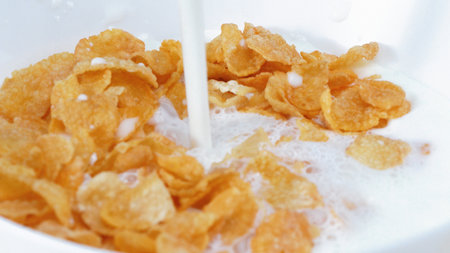Close up of a white bowl of cereal with milk being poured into it. Side view of white milk pouring...