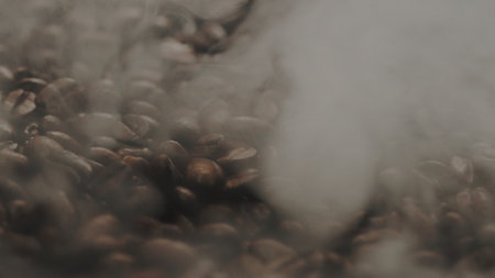 Close up of fresh brown coffee bean with roasted smoke from pile of coffee beans. Macrography of hot...