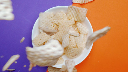 Top down aerial view of snack dropping and falling in to white bowl at separated blue and orange...