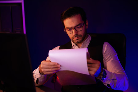 Serious smart businessman focusing on paperwork report folder analyzing sales channel disciplines product service comparing graph on pc screen market target customer at neon dark light room. Surmise.の写真素材