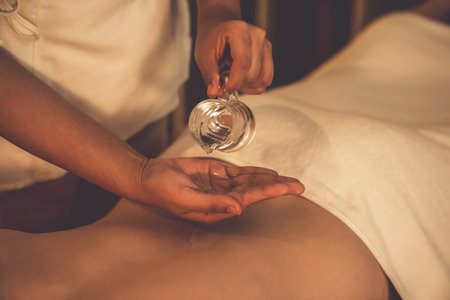 Closeup masseur hand pouring aroma oil on woman back. Masseuse prepare oil massage procedure for customer at spa salon in luxury resort. Aroma oil body massage therapy concept. Quiescentの写真素材