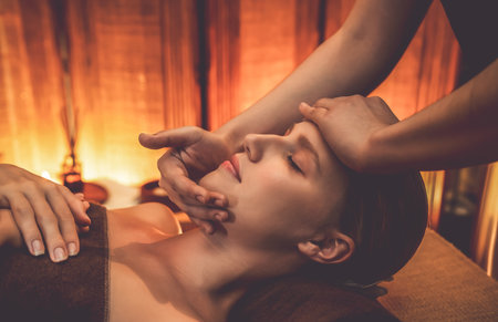 Caucasian woman enjoying relaxing anti-stress head massage and pampering facial beauty skin recreation leisure in warm candle lighting ambient salon spa in luxury resort or hotel. Quiescentの写真素材