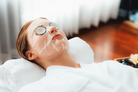 Serene daylight ambiance of spa salon, woman customer indulges in rejuvenating with luxurious cucumber facial mask. Facial skincare treatment and beauty care concept. Quiescentの写真素材