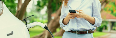 Panorama young woman recharge EV electric vehicle battery from EV charging station and using...