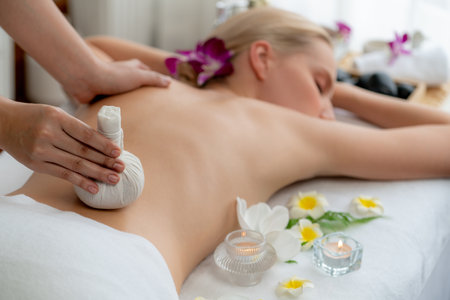Hot herbal ball spa massage body treatment, masseur gently compresses herb bag on woman body. Tranquil and serenity of aromatherapy recreation in day lighting ambient at spa salon. Quiescentの写真素材