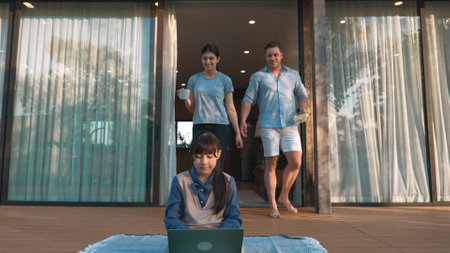 Father, mother and daughter focus laptop at terrace with garden view outside house. Parent use...