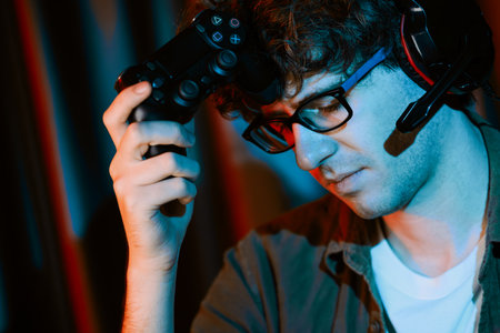 Stressful young gaming streamer team playing with joystick of Esport online on computer fighting harder lost game with to try winner on strategy plan for next at rad neon lighting modern room. Gusher.の写真素材