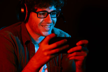 Smiling young gaming streamer team playing with Esport online on smartphone fighting wearing...