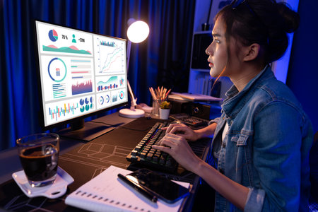 Smiling young beautiful asian creative looking on pc of profit of sales target report and writing on notebook for memo with planning invest new strategy market project at neon light night. Stratagem.の写真素材