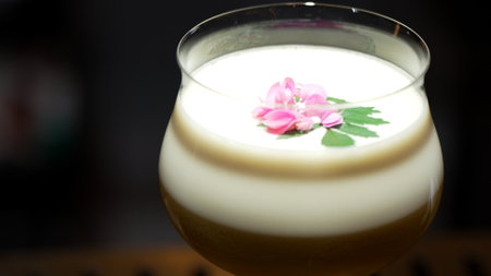 Closeup rotating in passion fruit smoothy cocktail glass serving special refreshing drink garnished with pink flower on smooth fizzy in showcasing nightlife mixology at luxurious nightclub. Vinosity.の写真素材