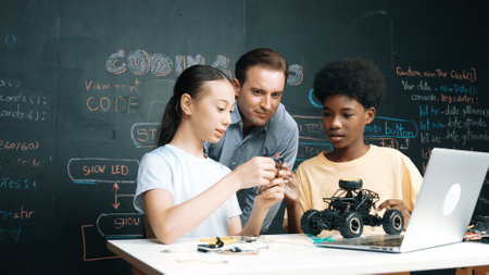 Caucasian teacher looking at laptop screen while explain car model system at blackboard with coding or programing code written. Happy diverse student learning about robotic construction. Edification.の写真素材