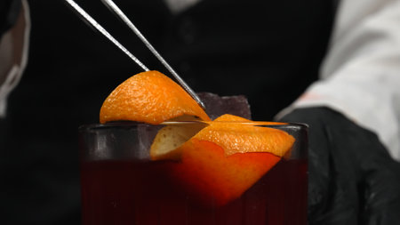 Macrography, skilled hands of a bartender decorate a Negroni cocktail, adorned with a vibrant orange...
