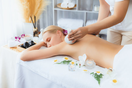 Hot herbal ball spa massage body treatment, masseur gently compresses herb bag on woman body. Tranquil and serenity of aromatherapy recreation in day lighting ambient at spa salon. Quiescentの写真素材