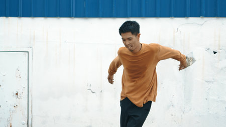 Hispanic man stretch arms and dance break dancing in front of wall. Motion shot of stylish street dancer in casual outfit practicing dancing in hip hop style. Outdoor sport 2023. Background. Hiphop.の写真素材