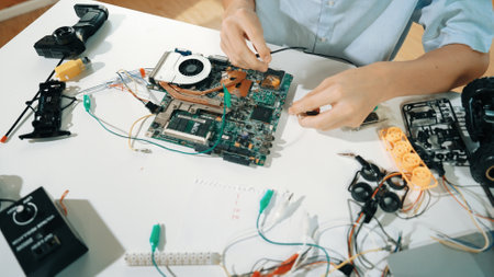 Closeup of boy hand fixing motherboard with electronic tool on table. Top view of highschool student repair electric board with electronic equipment, wires tool scatter around on table. Edification.の写真素材