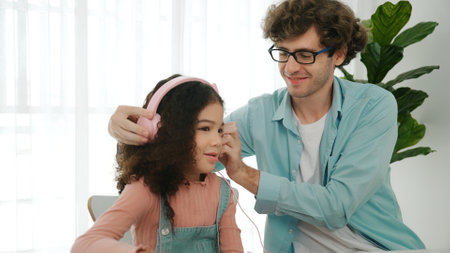 Caucasian dad put headphones on daughter while girl learning code. Father take care schoolgirl while...