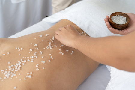 Blissful man customer having exfoliation treatment in luxury spa salon with warmth candle light ambient. Salt scrub beauty treatment in health spa body scrub. Quiescentの写真素材