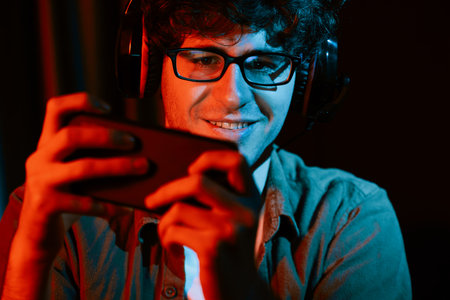 Smiling young gaming streamer team playing with Esport online on smartphone fighting wearing...