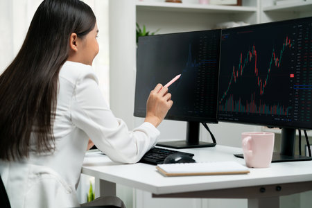 Young beautiful Asian businesswoman looking on pc to analyze profitable of exchange stock market...