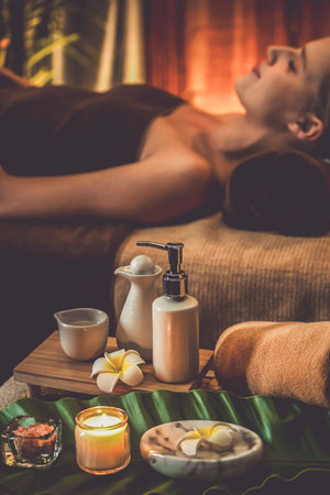 Aromatherapy massage ambiance or spa salon composition setup with focus decor candles and spa accessories on blurred woman enjoying blissful aroma spa massage in resort or hotel background. Quiescentの写真素材