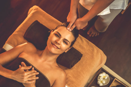 Caucasian woman enjoying relaxing anti-stress head massage and pampering facial beauty skin recreation leisure in warm candle lighting ambient salon spa in luxury resort or hotel. Quiescentの写真素材