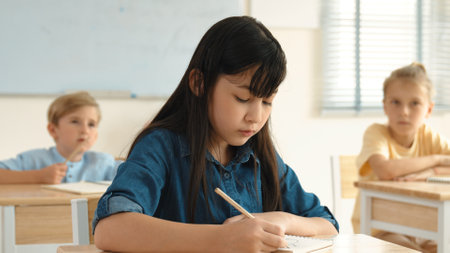 Asian girl writing answer in paper while focus on thinking about theory during test. Diverse smart students taking a note or lecturing while teacher teaching in elementary class. Education. Pedagogy.の写真素材