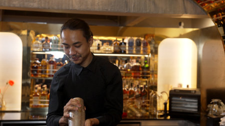 Asian smart bartender shaking mixed cocktail preparing to serve at luxurious counter preparation,...