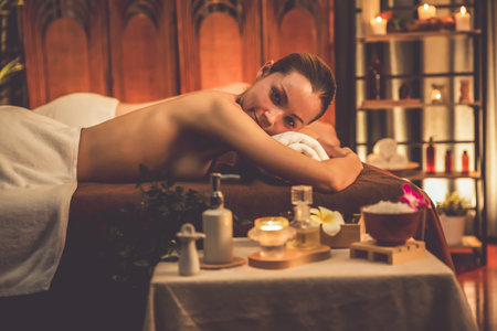 Aromatherapy massage ambiance or spa salon composition setup with focus decor candles and spa accessories on blurred woman enjoying blissful aroma spa massage in resort or hotel background. Quiescentの写真素材