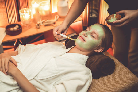 Serene ambiance of spa salon, woman customer indulges in rejuvenating with luxurious face cream massage with warm lighting candle. Facial skin treatment and beauty care concept. Quiescentの写真素材