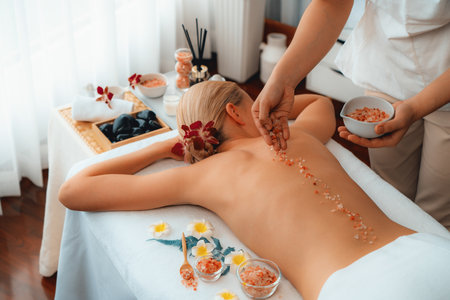 Woman customer having exfoliation treatment in luxury spa salon with warmth candle light ambient. Salt scrub beauty treatment in health spa body scrub. Quiescentの写真素材