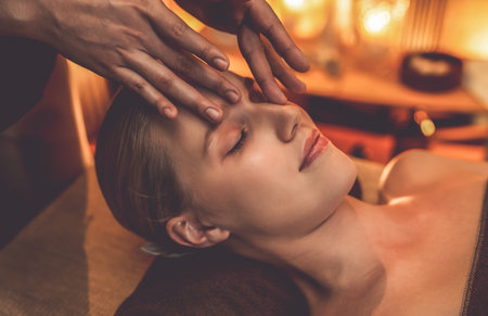 Closeup caucasian woman enjoying relaxing anti-stress head massage and pampering facial beauty skin recreation leisure in warm candle lighting ambient salon spa in luxury resort or hotel. Quiescentの写真素材