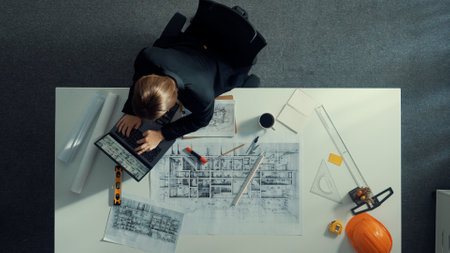 Top view of businesswoman look at blueprint. Engineer sit at meeting table with project plan, equipment and safety helmet. Aerial view of manager explain about building construction. Alimentation.の写真素材