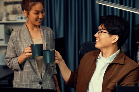 Sales managers discussing while drinking coffee cup together at over late night at home office, concept of modern working place with business report at breaking time with coworker at desk. Infobahn.の写真素材