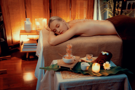 Woman customer having exfoliation treatment in luxury spa salon with warmth candle light ambient. Salt scrub beauty treatment in Health spa body scrub. Quiescentの写真素材