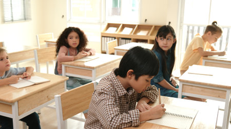 Asian skilled student working on classwork or doing test while sitting at classroom. Diverse children writing at paper or taking a note while attend in classroom. Elementary school concept. Pedagogy.の写真素材