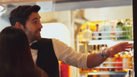 Smiling smart bartender providing excellent service to beautiful guest woman at back side vibrant nightlife party atmosphere in engaging lively conversation with VIP customer at nightclub . Vinosity.の写真素材