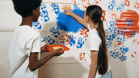 Diverse happy highschool girl and african boy paint the wall with water color in red and blue or contrast color by using their hands in art lesson. Colorful. Creative activity concept. Edification.の写真素材